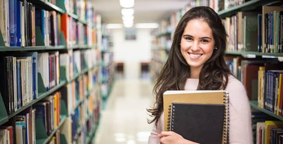 In the library - pretty female student with books working in a high school library.